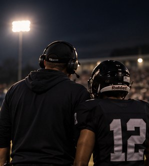 A football coach in a headset beside a player under the lights
